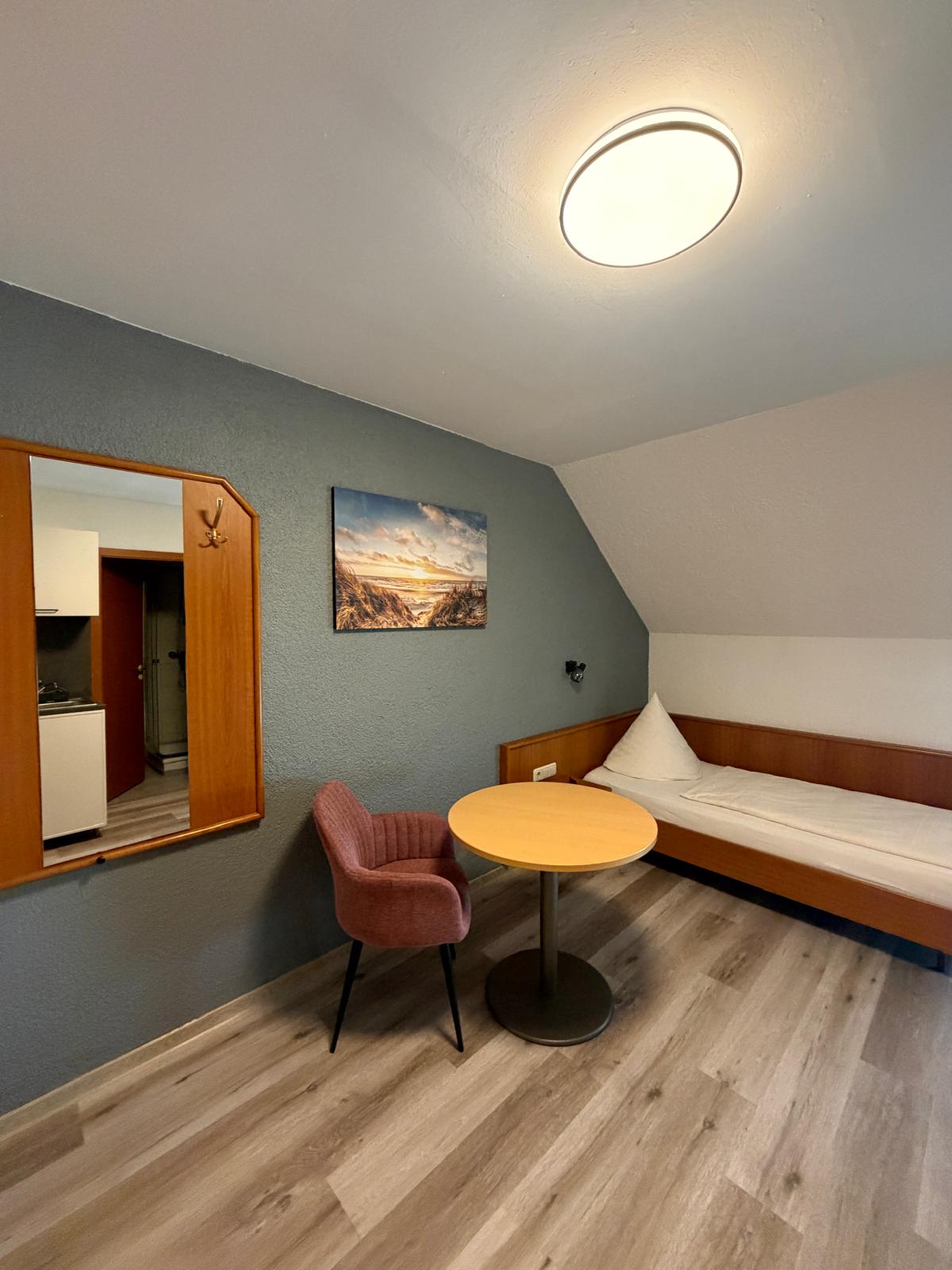 Single room under the sloped ceiling with table and armchair at Hotel Weller Riedstadt