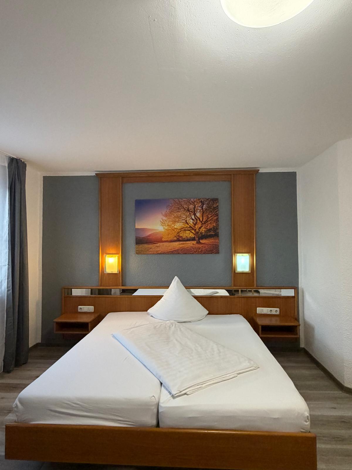 Cosy double bed with tree mural and warm reading lamps at Hotel Weller Riedstadt
