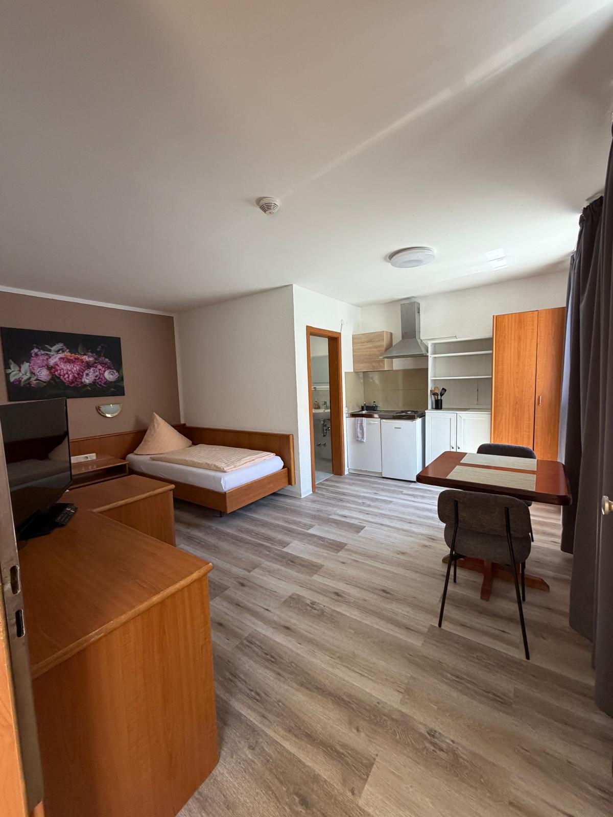 Apartment with wooden bed, TV, kitchenette and dining table at Hotel Weller Riedstadt